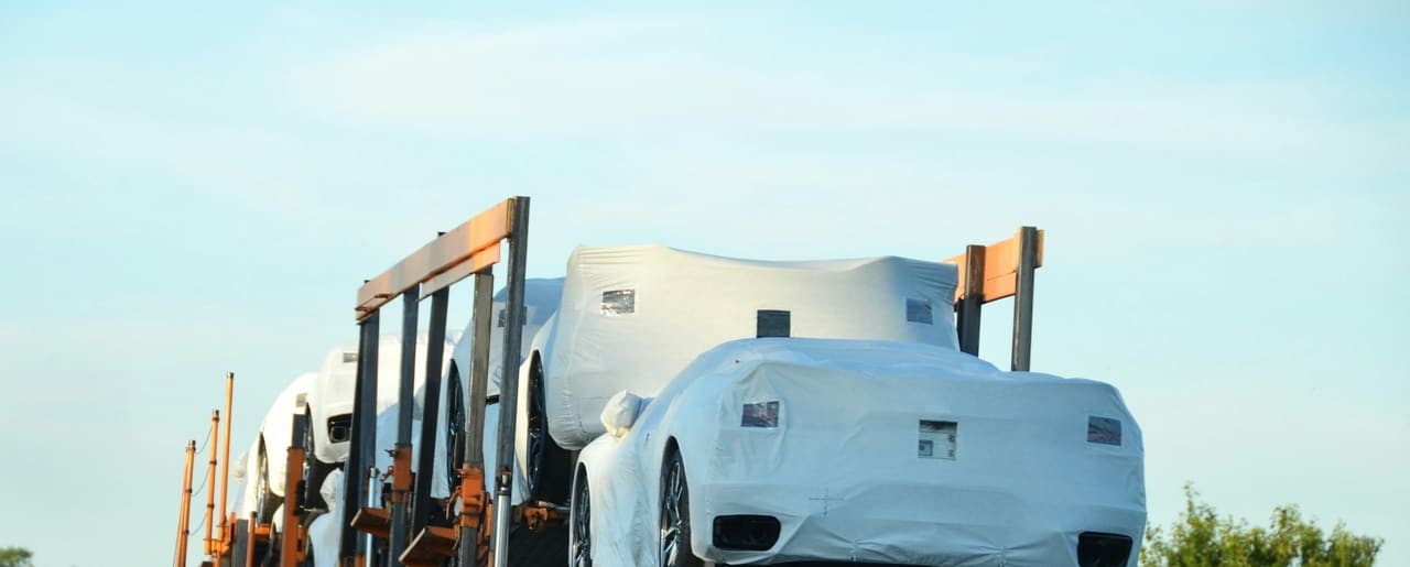 The upper and lower decks of a loaded car carrier running against open sky, covered vehicles held between the uprights.