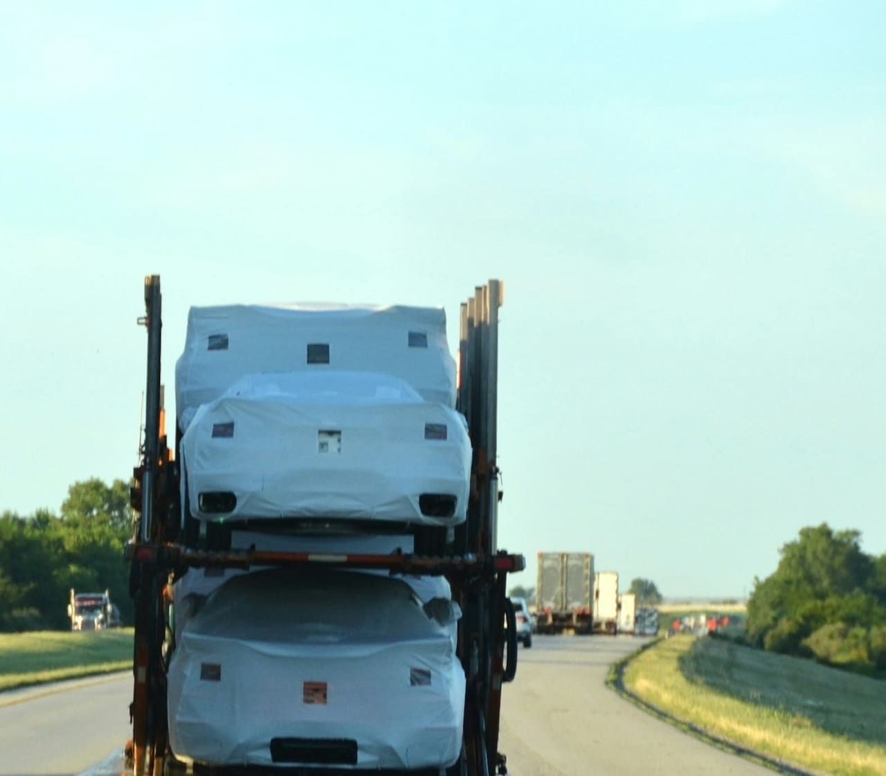 Covered vehicles riding on a car carrier in transit, deck rails and tie-downs visible along the trailer.