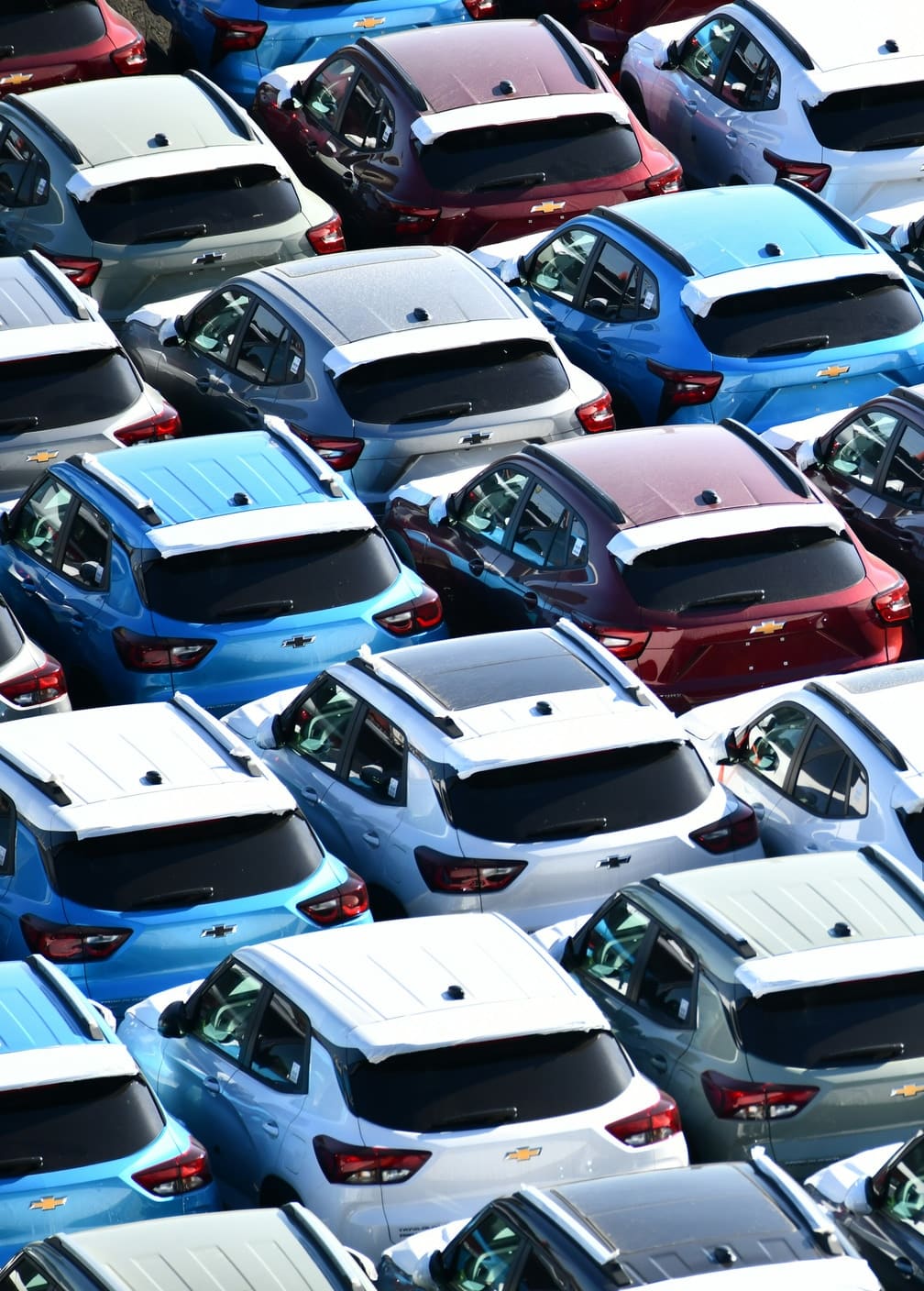 New vehicles ranked in a staging lot under white transit roof covers, seen down the length of the rows.