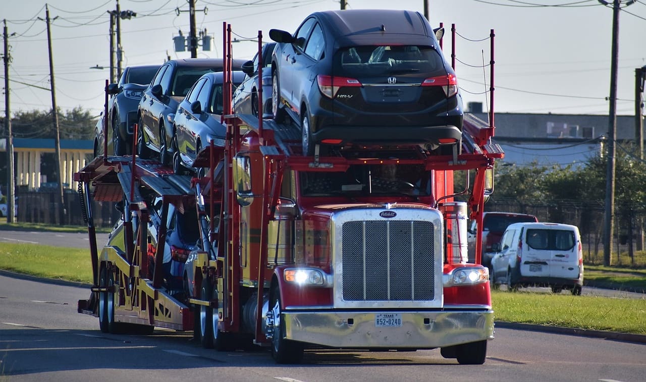 A loaded auto-transport rig head-on on a highway, vehicles filling both decks of the trailer behind it.