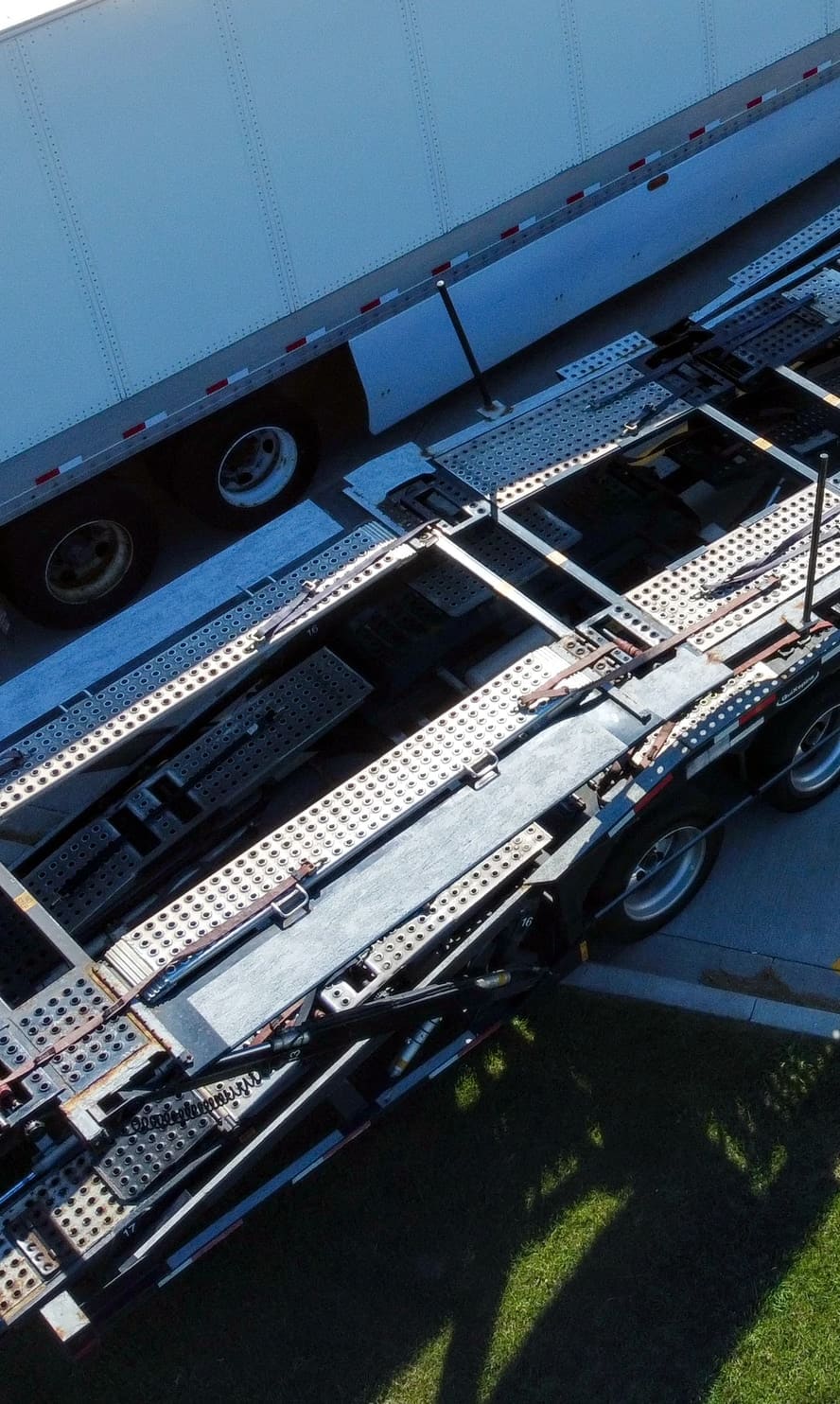 The loading ramps, grating and tie-down rails of a car carrier seen from above, running the length of the trailer.